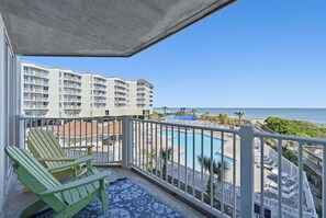 A balcony with a view of a swimming pool, beach, and hotel buildings.