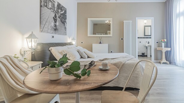 A modern hotel room with a bed, a round wooden table with a cup, a potted plant, and a large mirror. - Thea-historical center Monza (Monza)