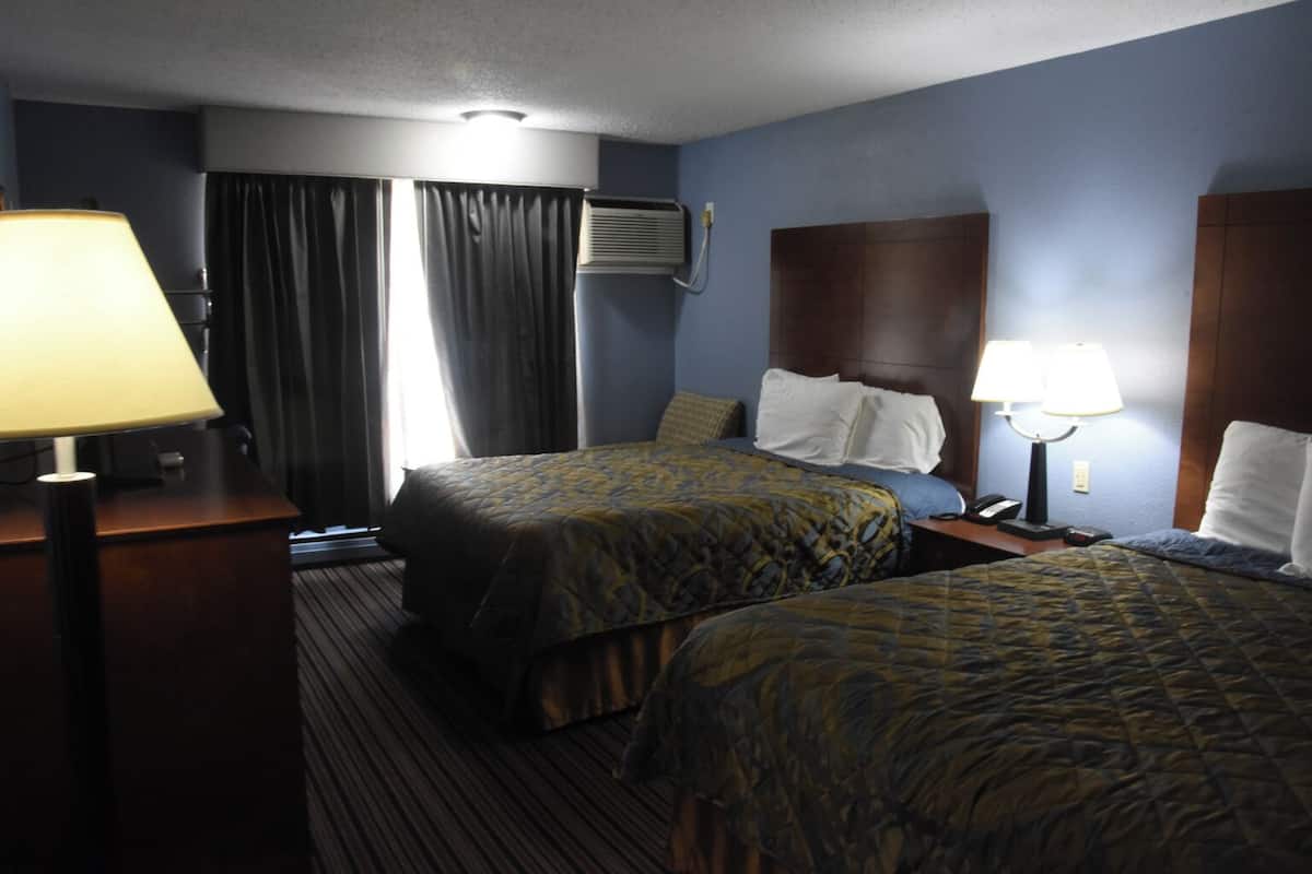 Una habitación de hotel con dos camas, un escritorio, una lámpara y una ventana con cortinas.