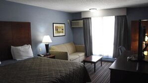 A hotel room with a large bed, a sofa, a desk, and a chair. There is a lamp, a picture on the wall, and an air conditioning unit. - Timber Motel (Clinton)