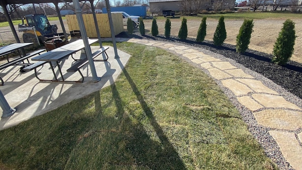 A covered patio area with picnic tables, a stone pathway, and a row of neatly trimmed shrubs. - Timber Motel (Clinton)