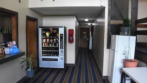 A hallway with a vending machine, a fire alarm, a refrigerator, and a potted plant. - Timber Motel (Clinton)