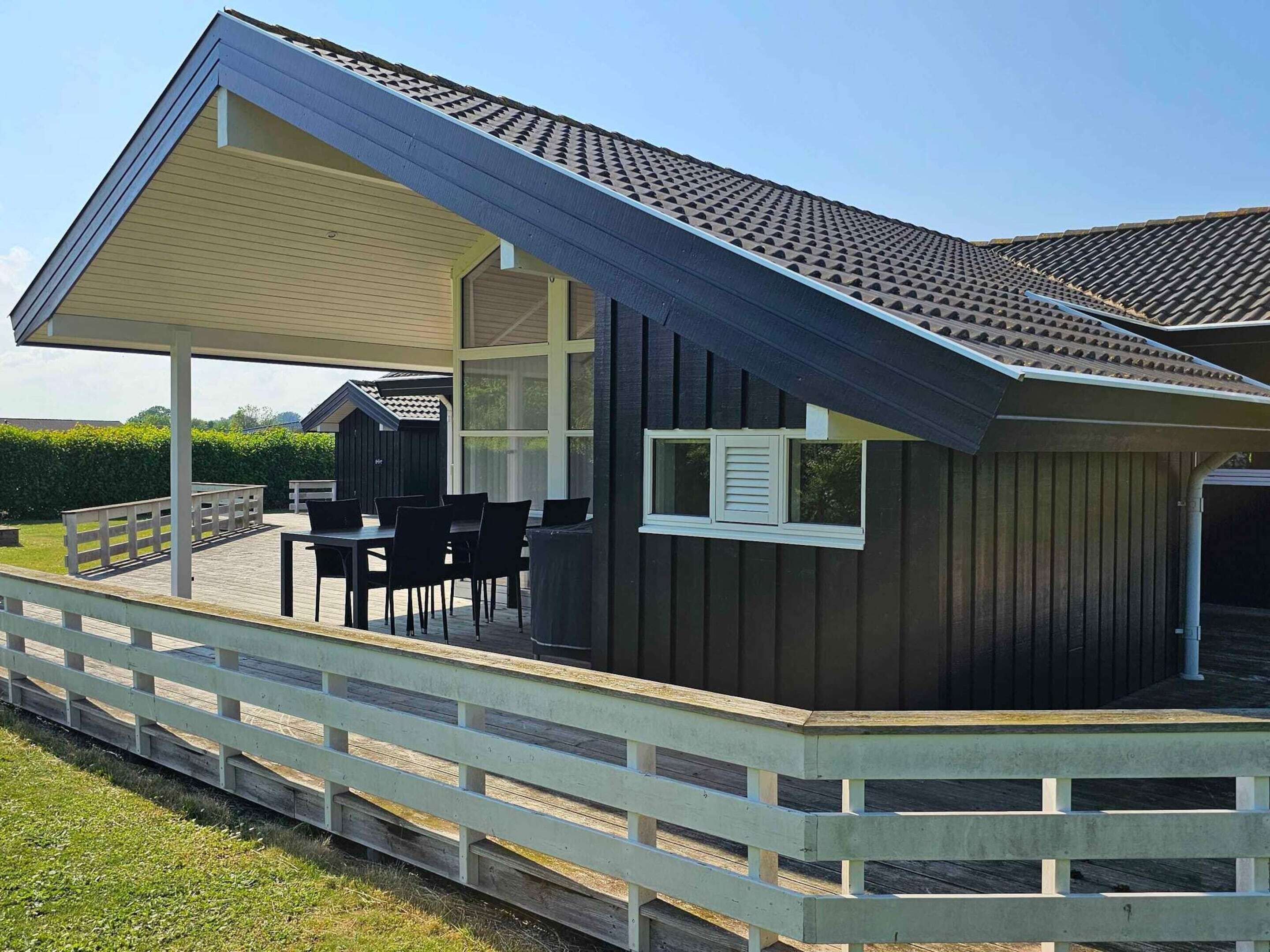 Ein modernes Haus mit überdachter Terrasse, einer kleinen Holzterrasse und einer Garage.