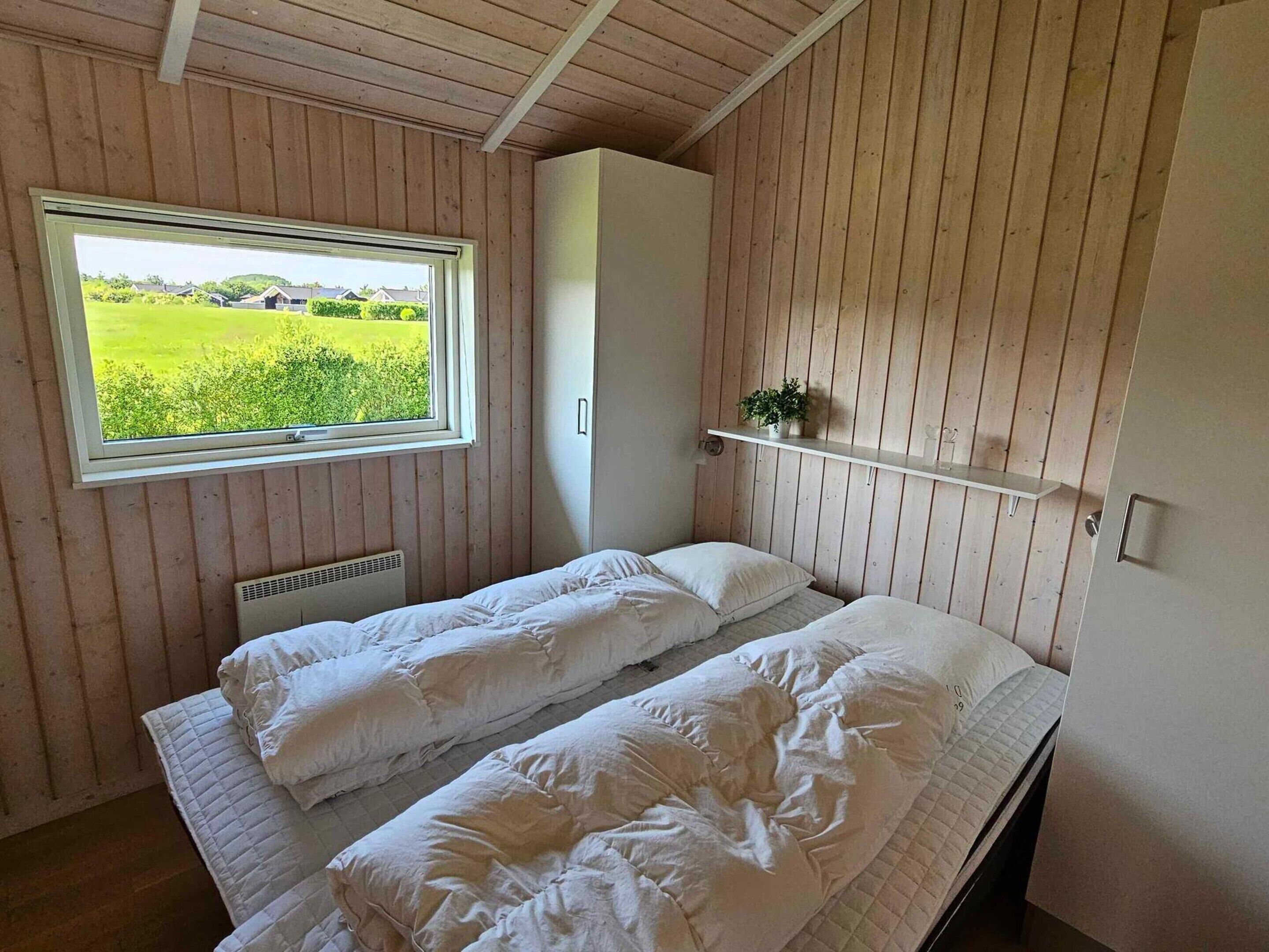 A bedroom with two beds, a window with a view of greenery, and a white wardrobe.