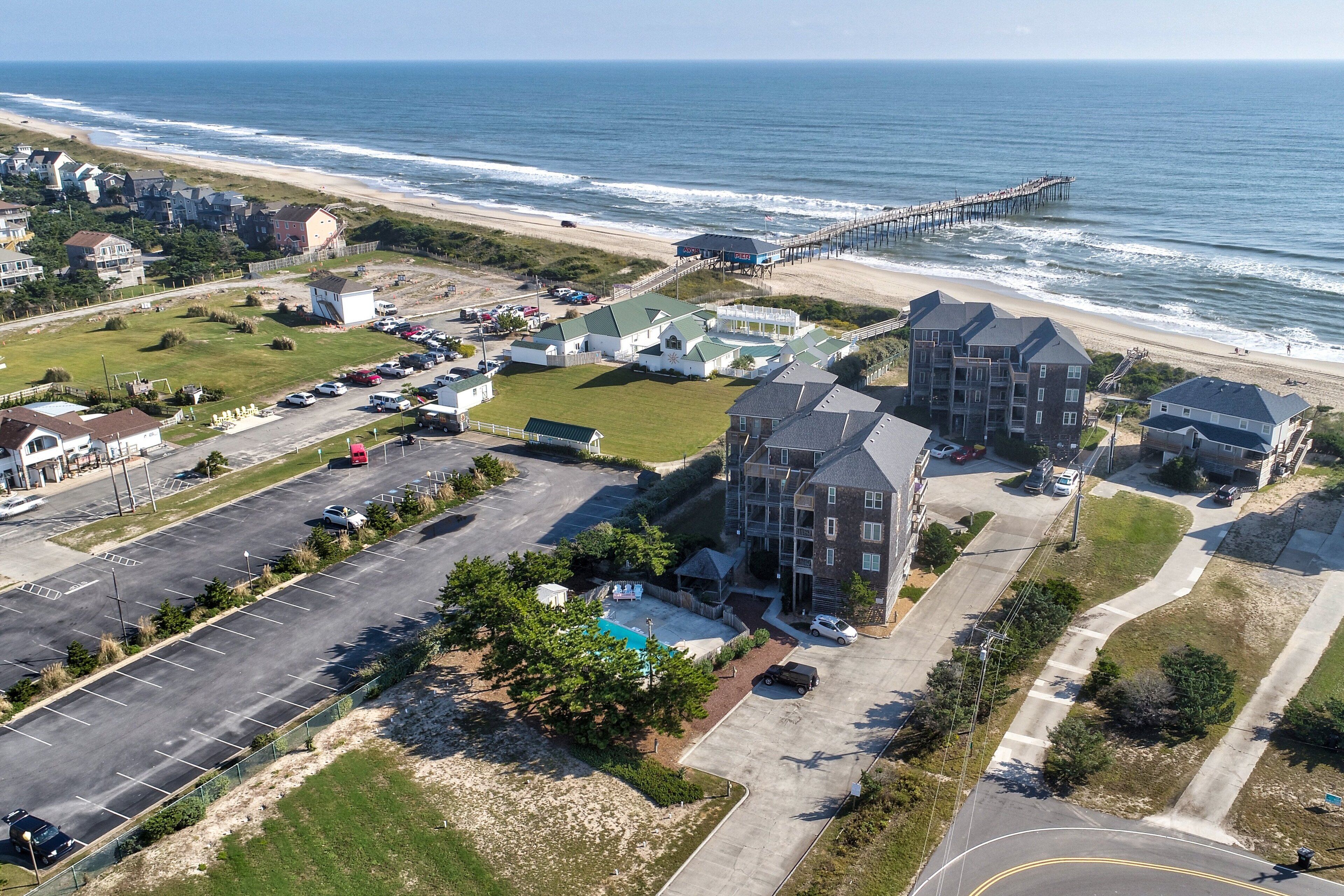 Vista aérea de una zona residencial costera con playa, muelle y estacionamiento.