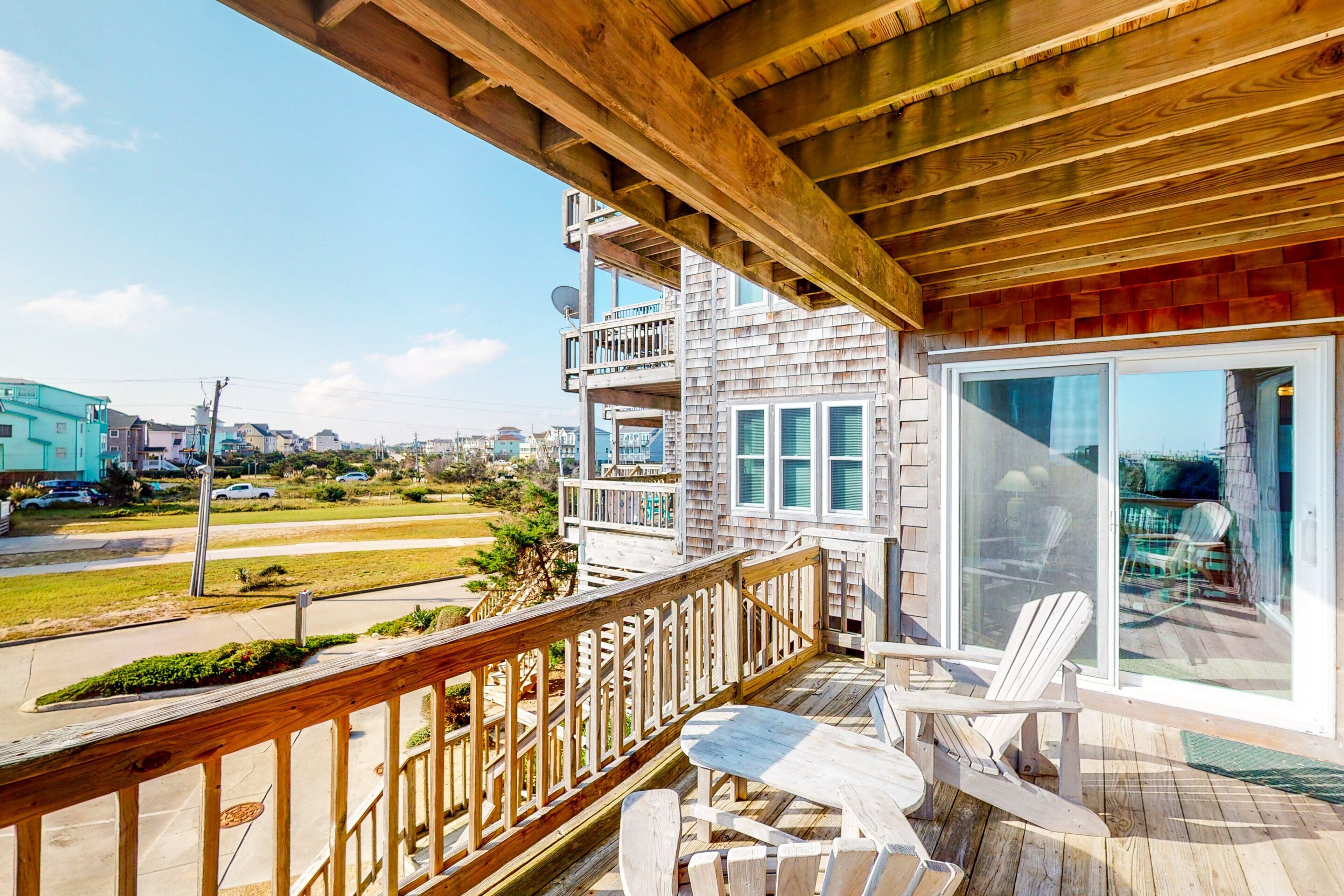 A wooden deck with a table and chairs, overlooking a residential area with houses and a road.