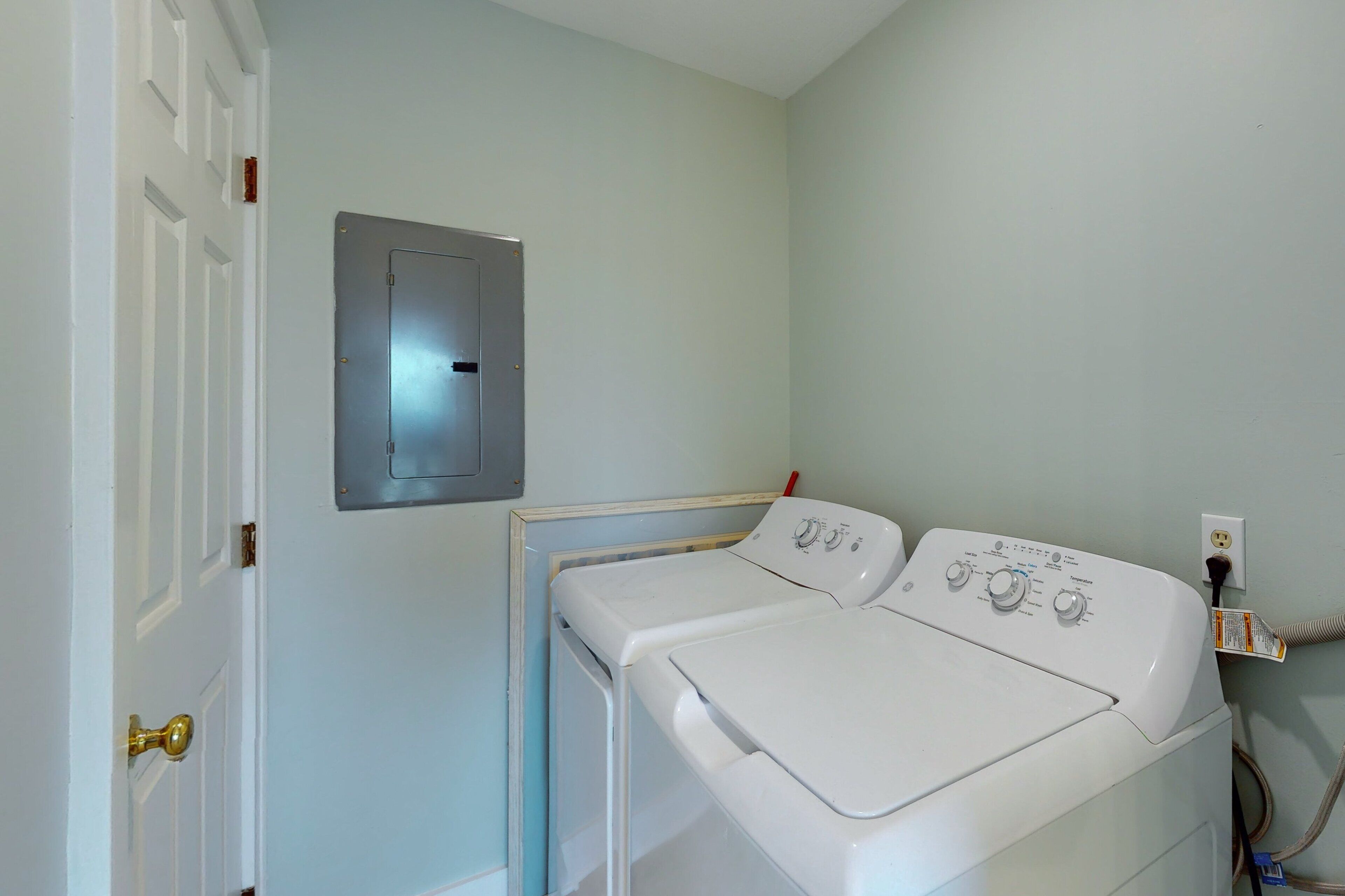 A laundry room with a front-loading washer and dryer, a door with a brass handle, and a wall-mounted electrical outlet.