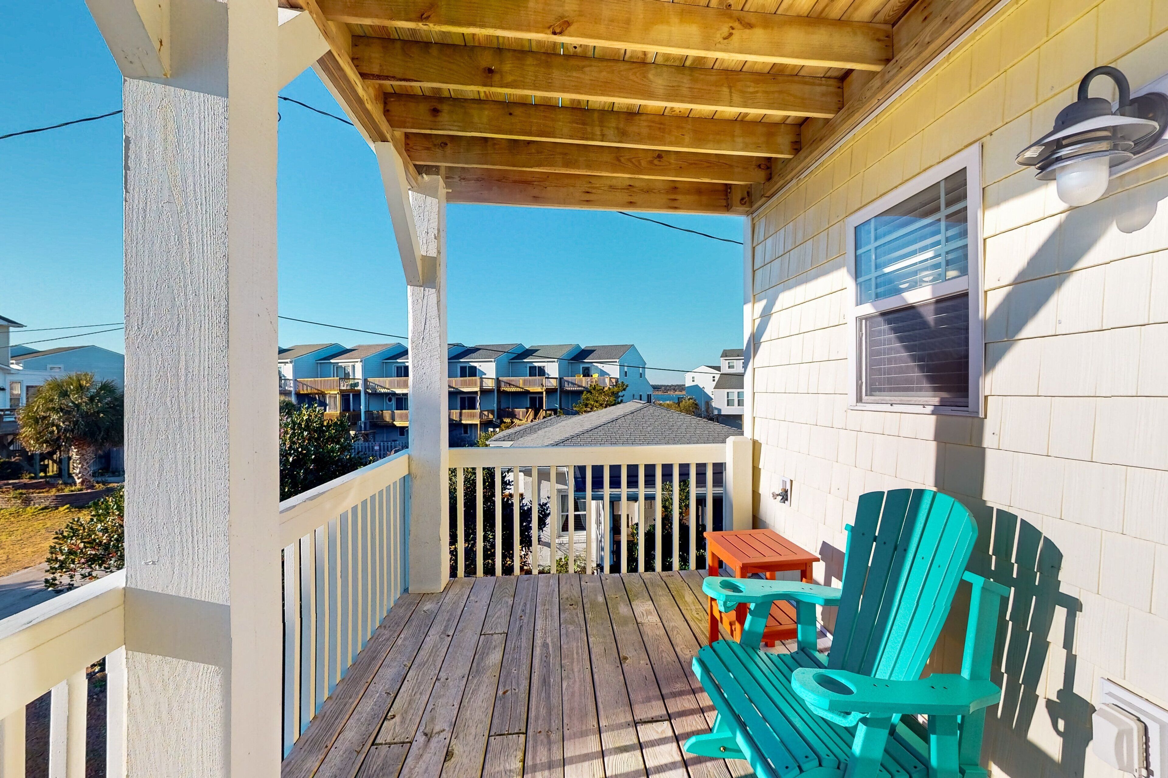 A wooden deck with a covered area, a turquoise Adirondack chair, and a small table.