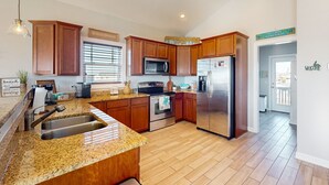 Una cocina moderna con encimeras de granito, electrodomésticos de acero inoxidable, armarios de madera y una isla grande con lavamanos.