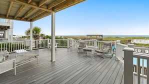 Eine Holzterrasse mit weißen Geländern, Gartenmöbeln und Blick auf den Strand.