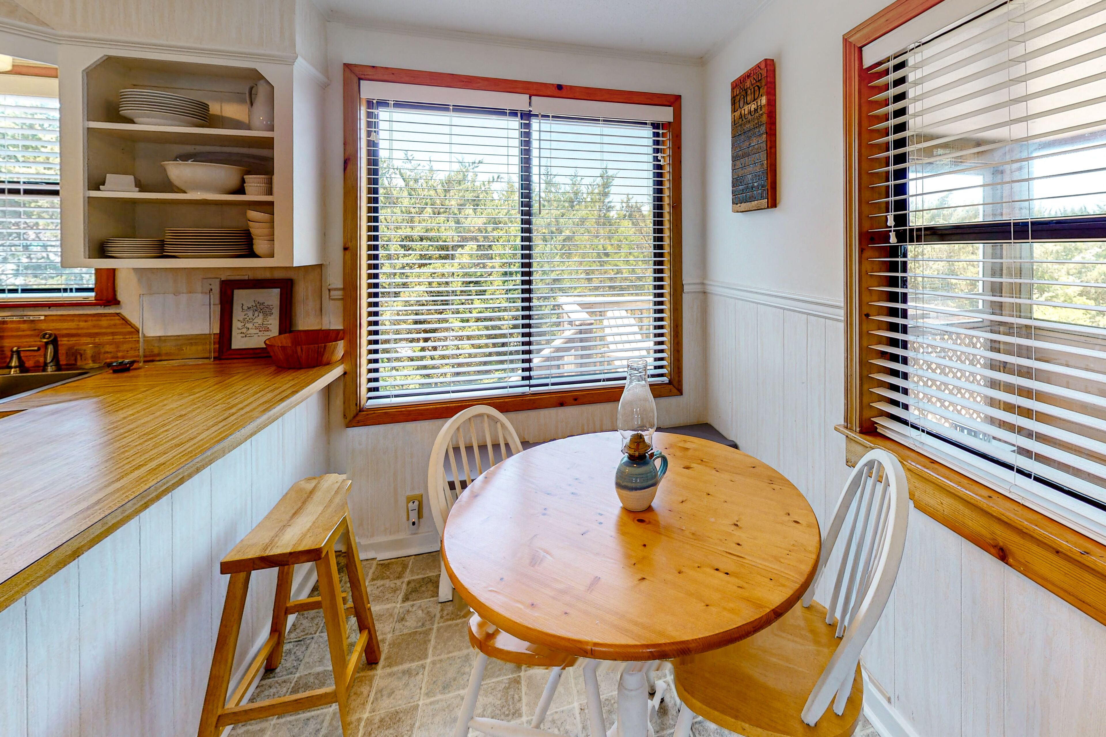 A kitchen with a wooden table and chairs, a built-in shelf with dishes, and a window with blinds.