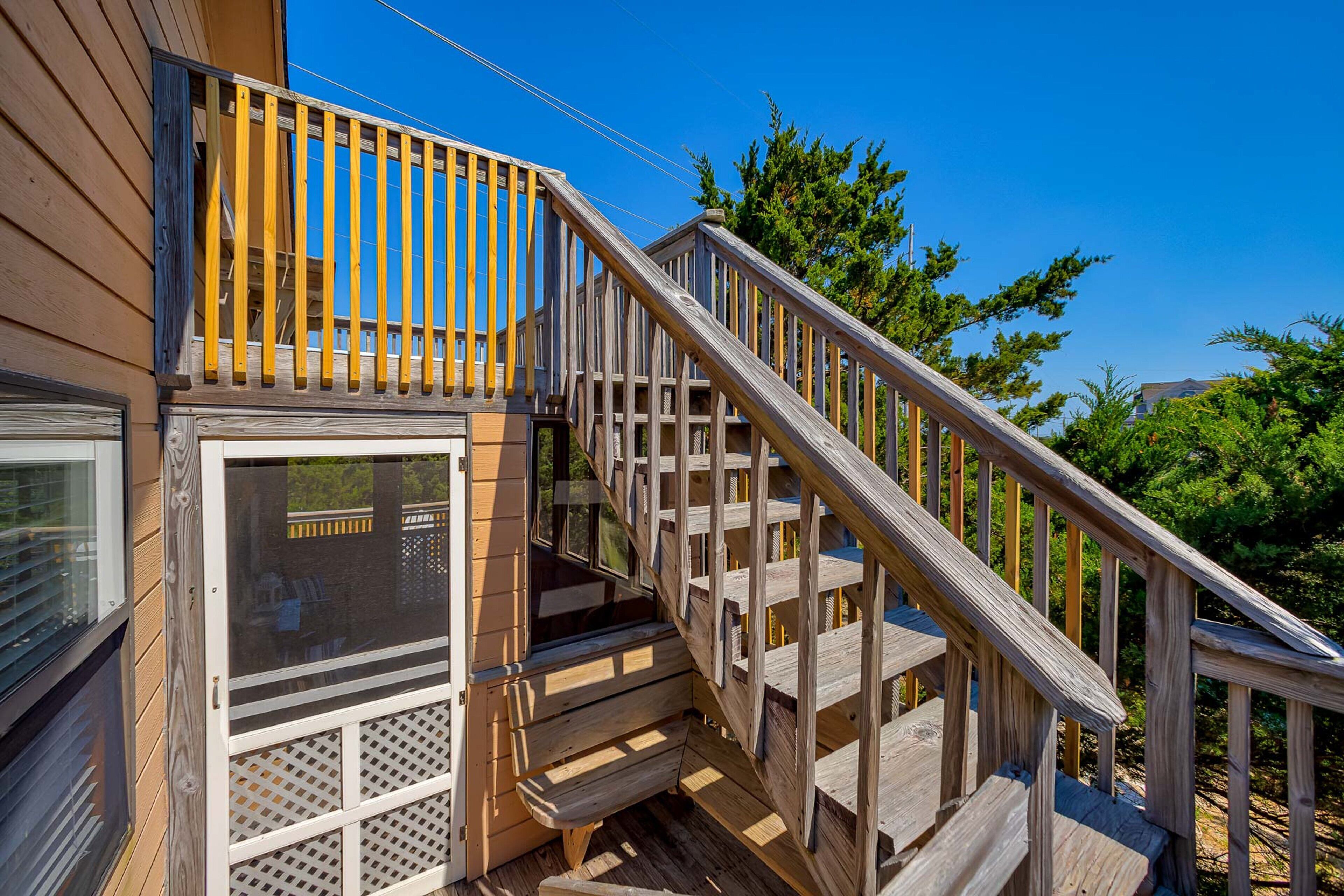 A wooden deck with a staircase leading to a covered area, surrounded by trees.