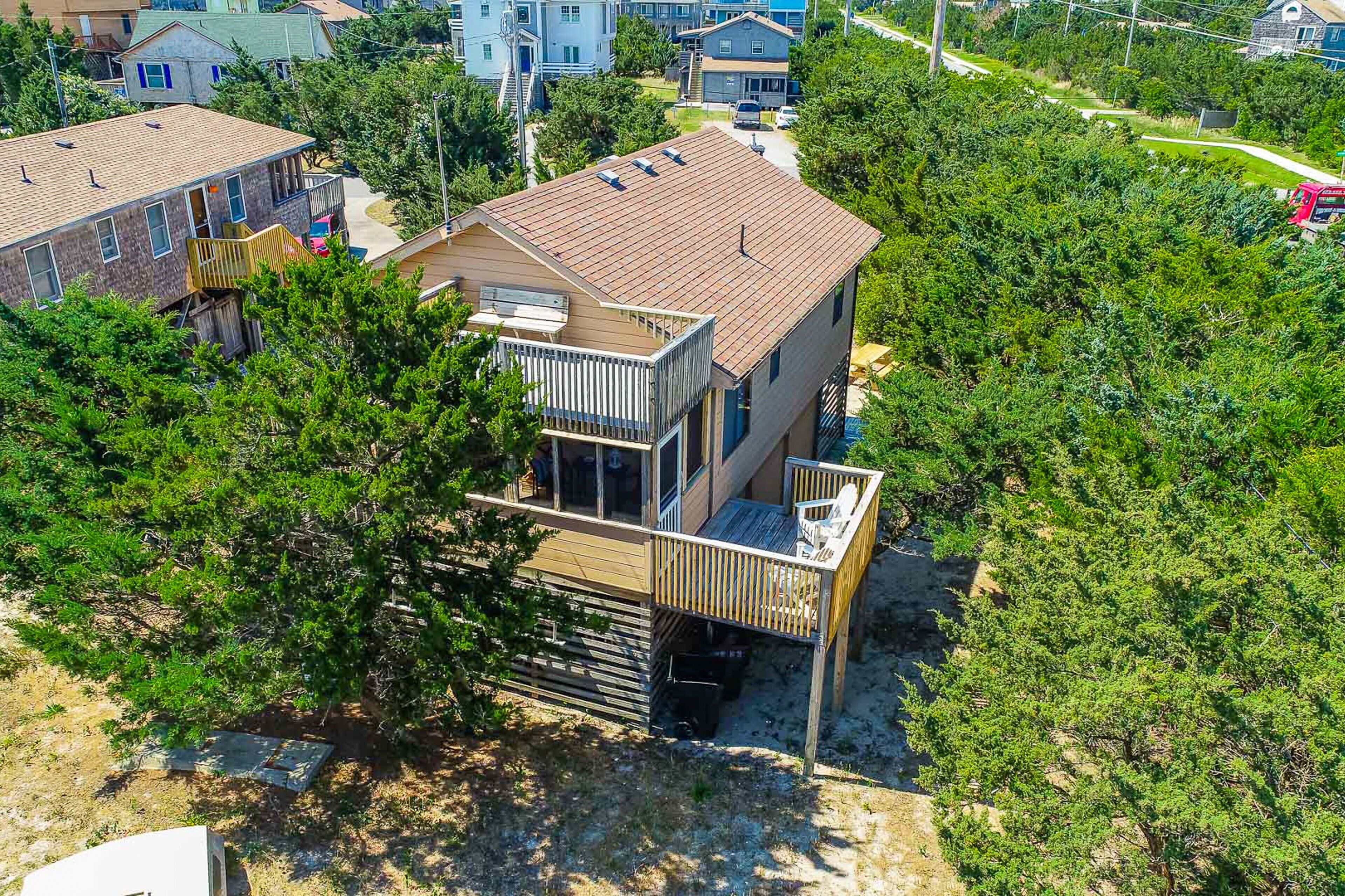 A two-story house with a balcony and a small deck, surrounded by trees and other houses.