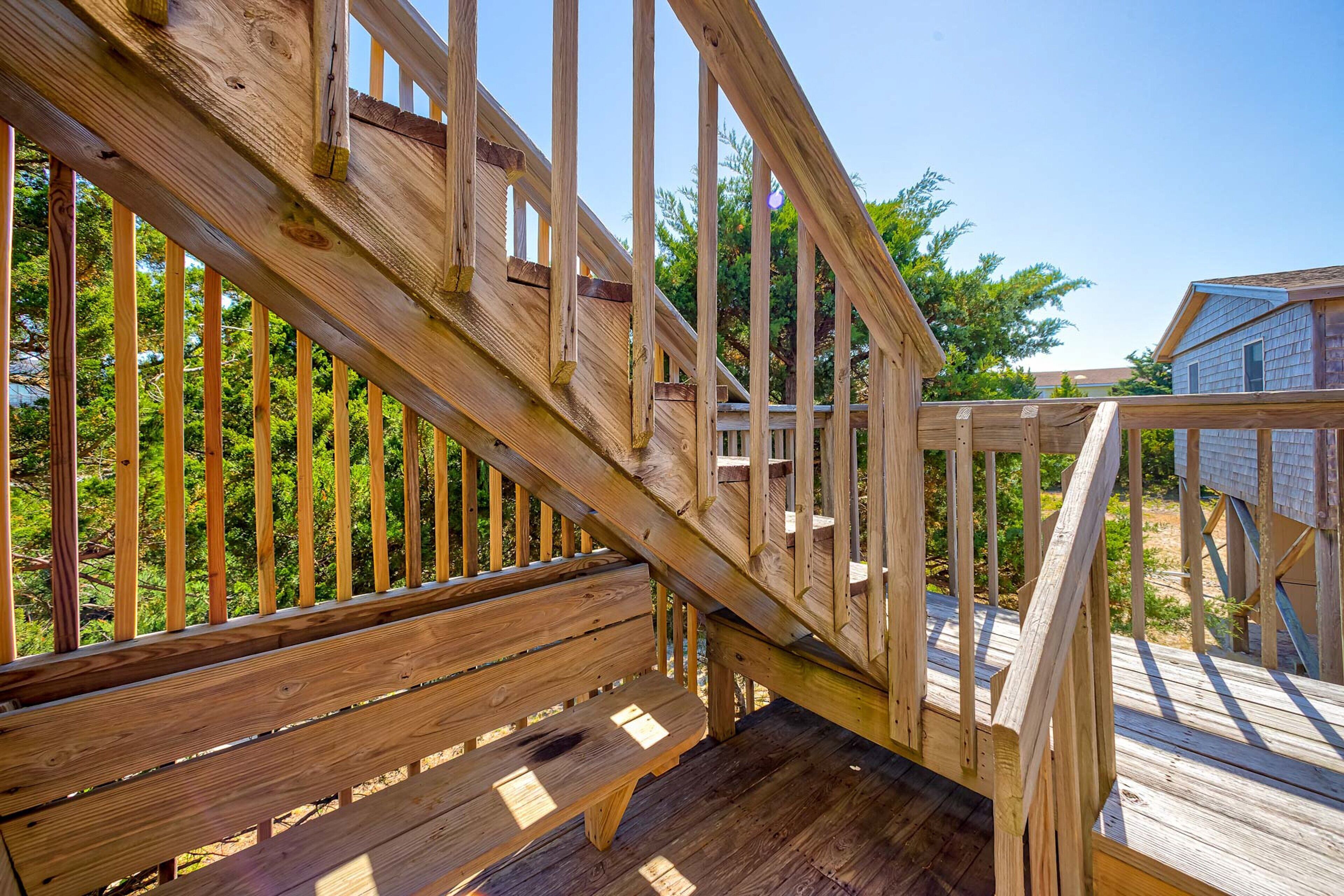 Una terraza de madera con un banco y una escalera que conduce a una casa.