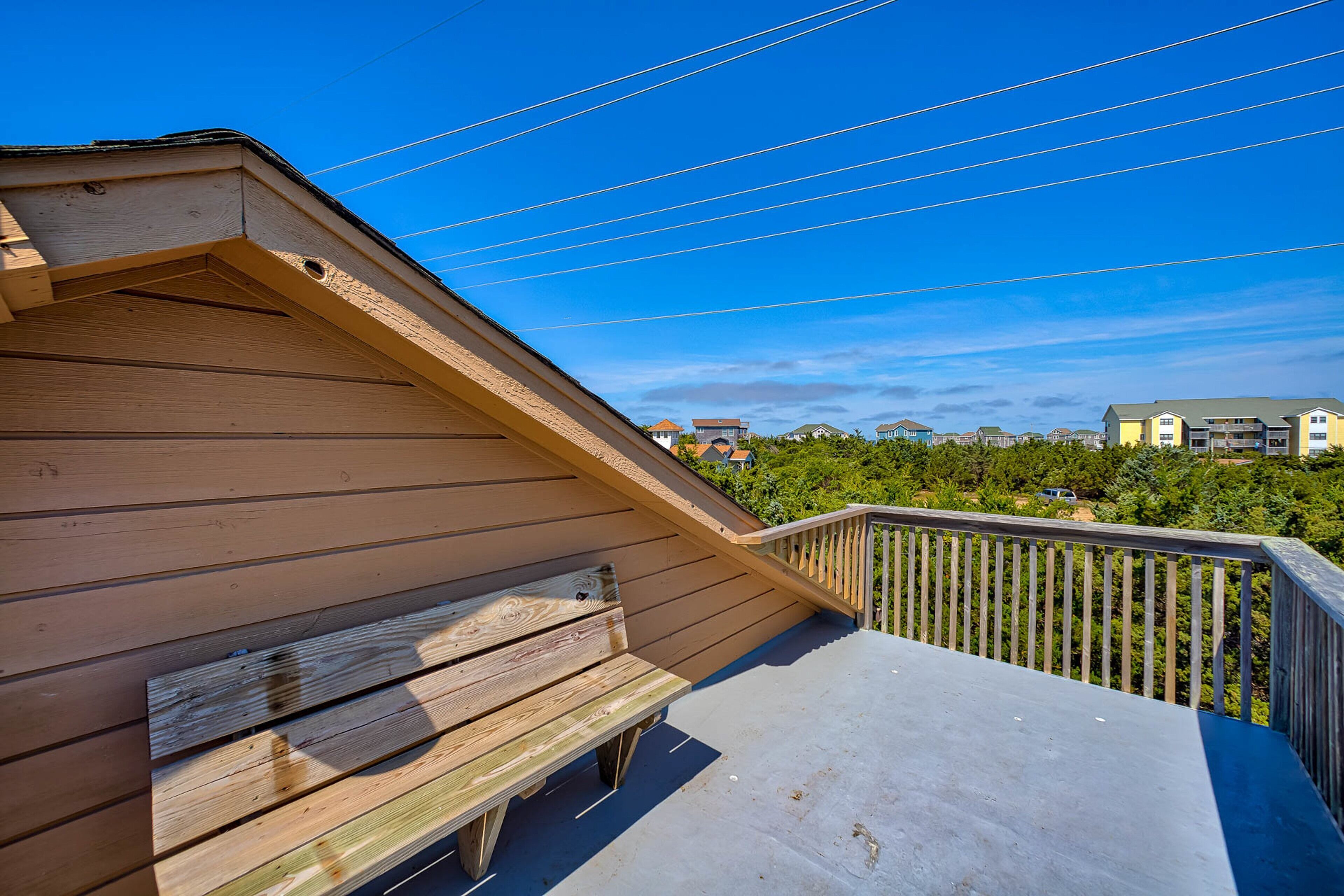 Une terrasse en bois avec un banc, une rambarde et une vue sur les bâtiments en arrière-plan.