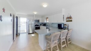 A modern kitchen with white cabinets, a central island with bar stools, and a dining area. - Stunning, Multi-Level Home Steps From Beach w/WiFi, Central AC, W/D, & Patio (Holden Beach)