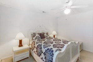 Een slaapkamer met een bed, twee nachtkastjes met lampen, een plafondventilator en een effen witte muur.