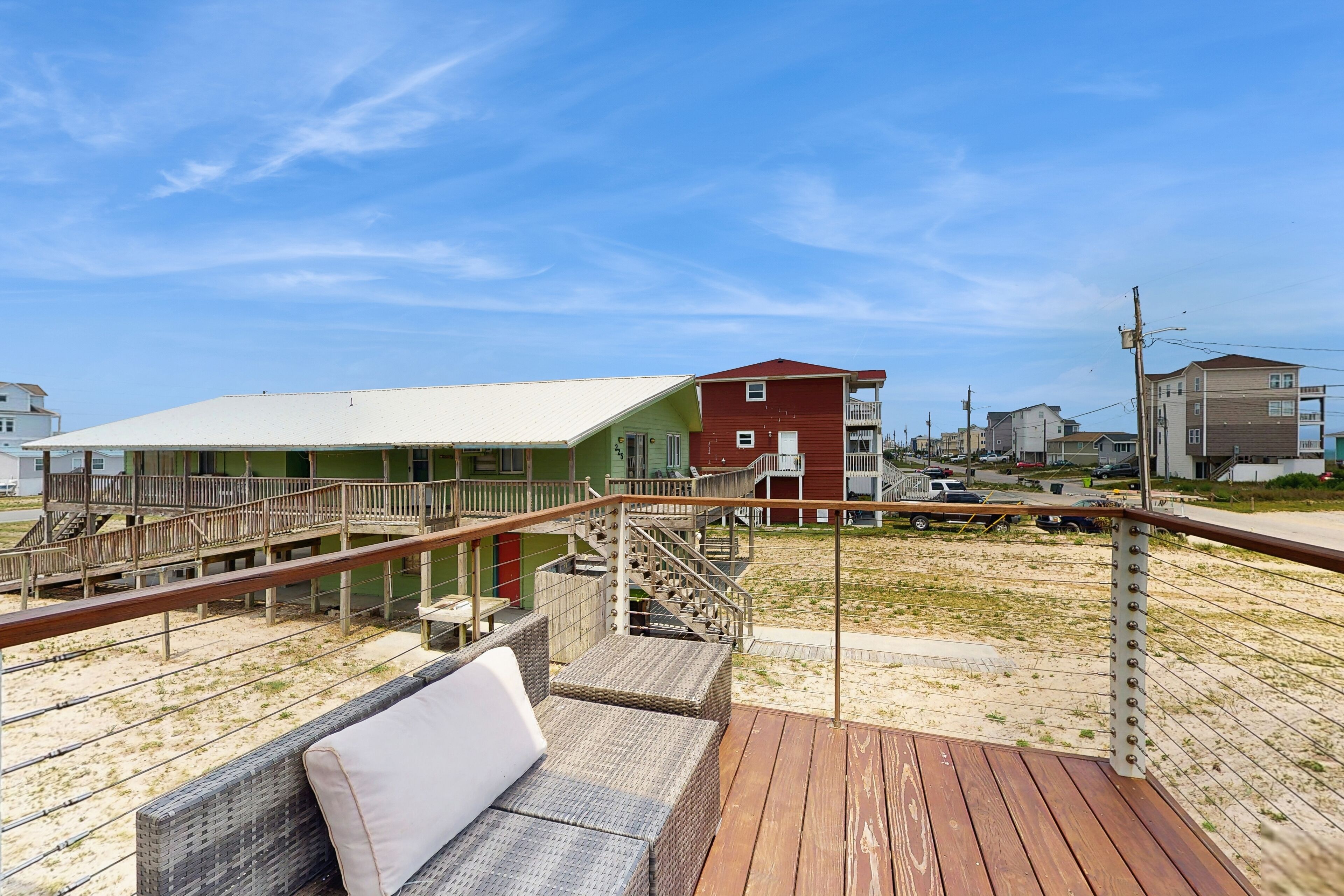 Eine Holzdar Terrasse mit Korbmöbeln und Blick auf Gebäude und einen Strand.