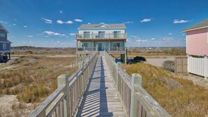 A wooden boardwalk leading to a two-story beach house with a balcony and a view of the beach. - Oceanfront home with great views, central AC, washer/dryer, beach access (North Topsail Beach)