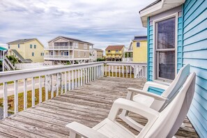 A wooden deck with white chairs and a railing, overlooking a row of colorful houses. - Fantastic house with WiFi, central AC, and private washer/dryer - steps to beach (Holden Beach)