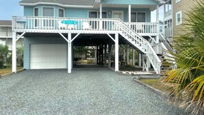 A two-story building with a covered entrance, a balcony, and a staircase leading to the upper level. - Fantastic house with WiFi, central AC, and private washer/dryer - steps to beach (Holden Beach)