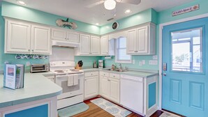 A kitchen with white cabinets, a blue door, and a ceiling fan. - Magnificent house with central AC, patio, deck, W/D & screened porch (Holden Beach)