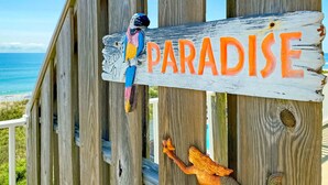 Uma placa de madeira com a palavra 'PARADISE' em letras negrito, uma figura de papagaio e uma pequena âncora de madeira.