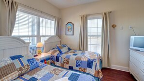 Quarto com duas camas, um ventilador de teto, televisão e janela com cortinas.
