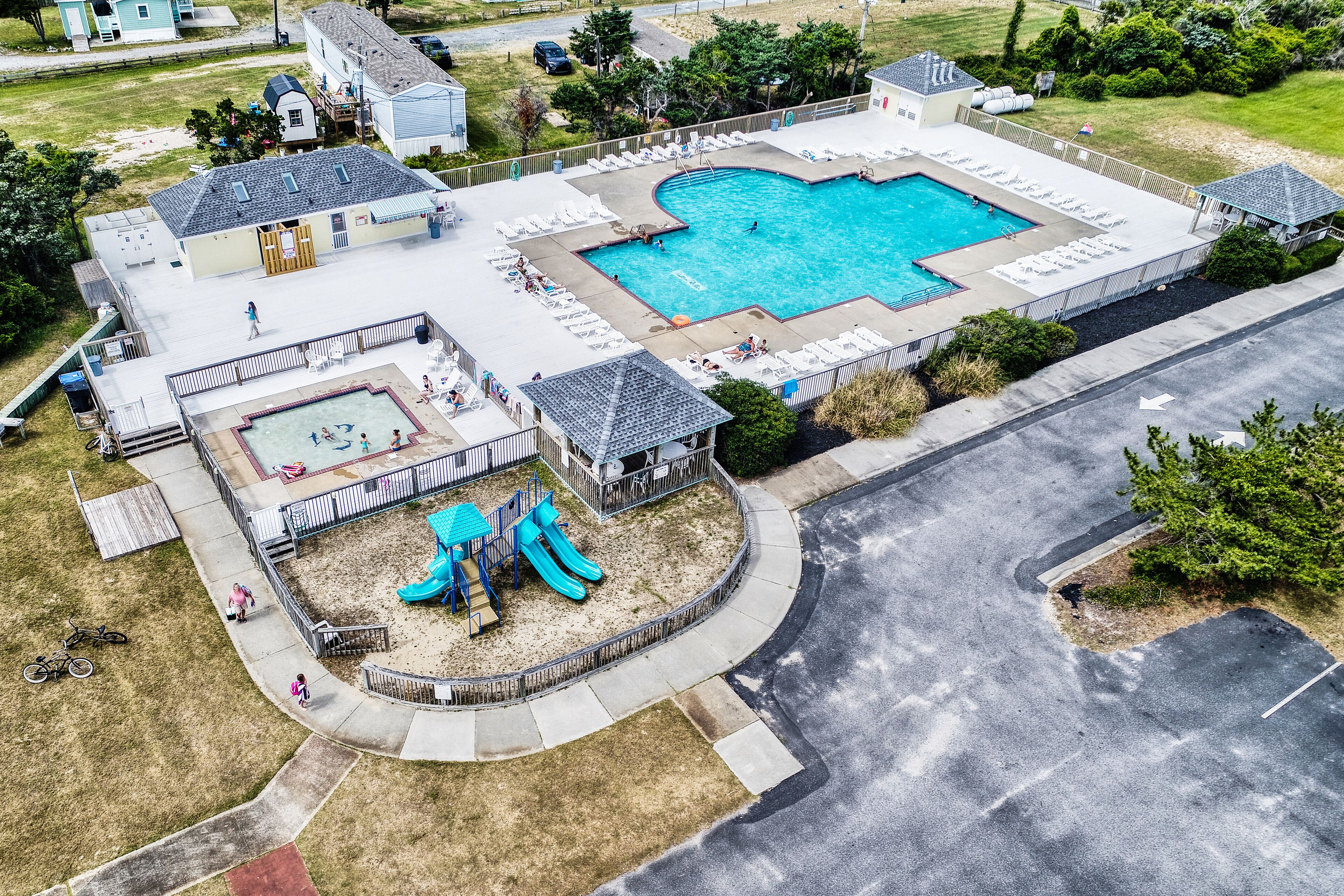 An aerial view of a residential area with a swimming pool, a children's play area with slides, and a small building with a porch.