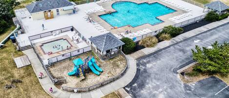 An aerial view of a residential area with a swimming pool, a children's play area with slides, and a small building with a porch.