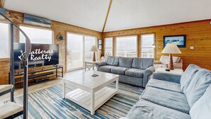 Un salon chaleureux avec un décor intérieur en bois, un téléviseur à écran plat, un canapé, une table basse et une vue dégagée grâce à de grandes fenêtres.