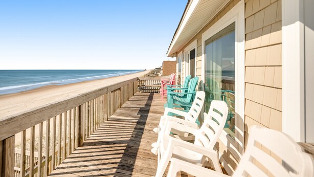 Une terrasse en bois avec des chaises de plage, une rambarde et une vue sur l’océan.