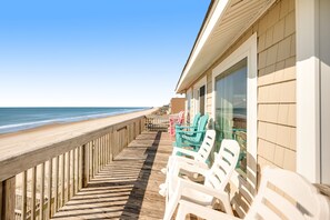 A wooden deck with beach chairs, a railing, and a view of the ocean.
