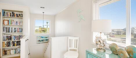 A room with a bookshelf, a white chair, a window with blinds, and a decorative lamp.