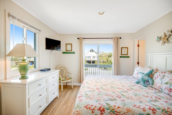 A bedroom with a bed, a dresser, a chair, a TV, and a balcony with a view.