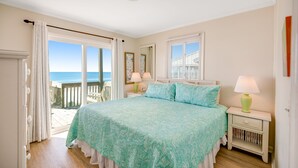 Une chambre avec un grand lit, une table de chevet, une lampe, une fenêtre donnant sur la mer et un balcon.