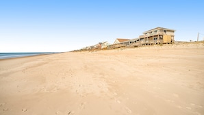 Une propriété située en bord de mer, comprenant plusieurs maisons, une plage de sable et un ciel bleu dégagé.