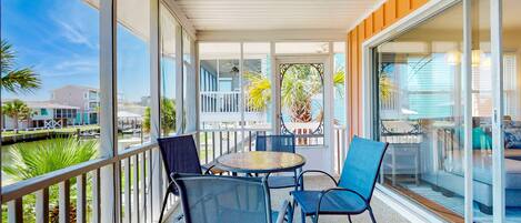 A covered outdoor seating area with a table and chairs, large windows, and a view of the surrounding area.