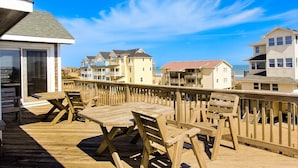 A wooden deck with outdoor furniture, overlooking a beachfront with multi-story buildings. - Waterfront house with pool, hot tub, pool table, elevator & ocean view (Buxton)