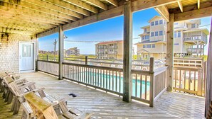 A wooden deck with a pool, wooden chairs, and a view of multi-story buildings. - Waterfront house with pool, hot tub, pool table, elevator & ocean view (Buxton)