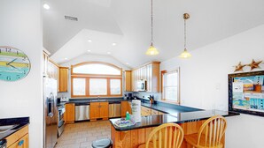 A kitchen with wooden cabinets, a black countertop, and a large window. - Waterfront house with pool, hot tub, pool table, elevator & ocean view (Buxton)