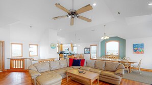 A spacious living room with a large L-shaped sectional sofa, a wooden coffee table, and a ceiling fan. - Waterfront house with pool, hot tub, pool table, elevator & ocean view (Buxton)