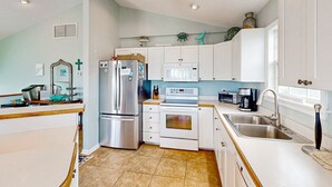A modern kitchen with white cabinets, stainless steel appliances, and a large window. - Inviting house with central AC, private pool, hot tub, ocean views, & W/D (Hatteras)