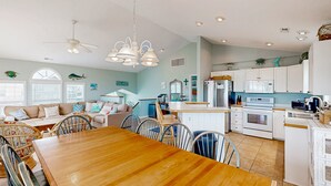 A spacious kitchen with white cabinets, a central island, and a dining area with a wooden table and chairs. - Inviting house with central AC, private pool, hot tub, ocean views, & W/D (Hatteras)