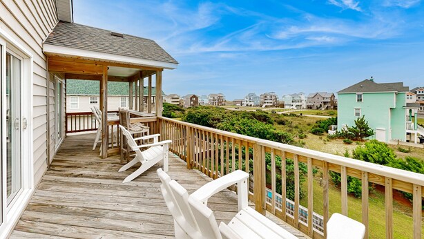 A wooden deck with white chairs and a covered area, overlooking a residential area with houses and greenery. - Inviting house with central AC, private pool, hot tub, ocean views, & W/D (Hatteras)