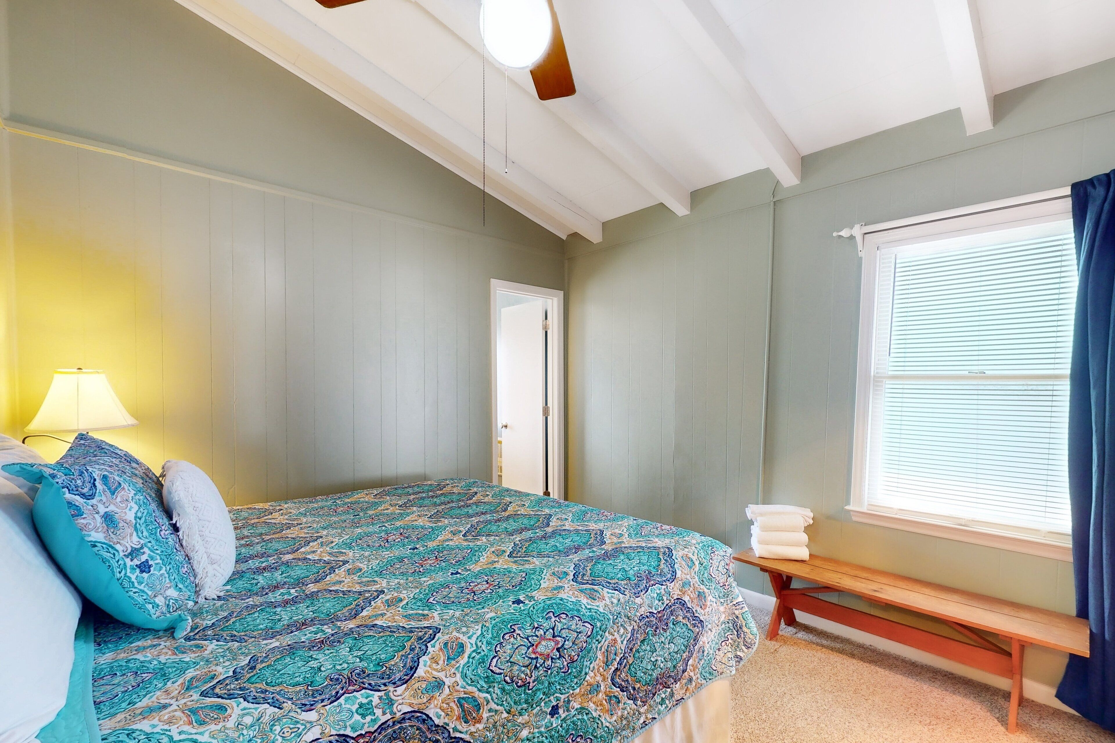 Une chambre à coucher avec une couvre-lit à motifs, un banc près de la fenêtre et une lampe sur le côté gauche.