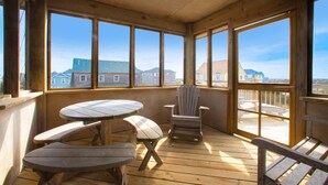 A wooden deck with a table and chairs, large windows, and a view of buildings.
