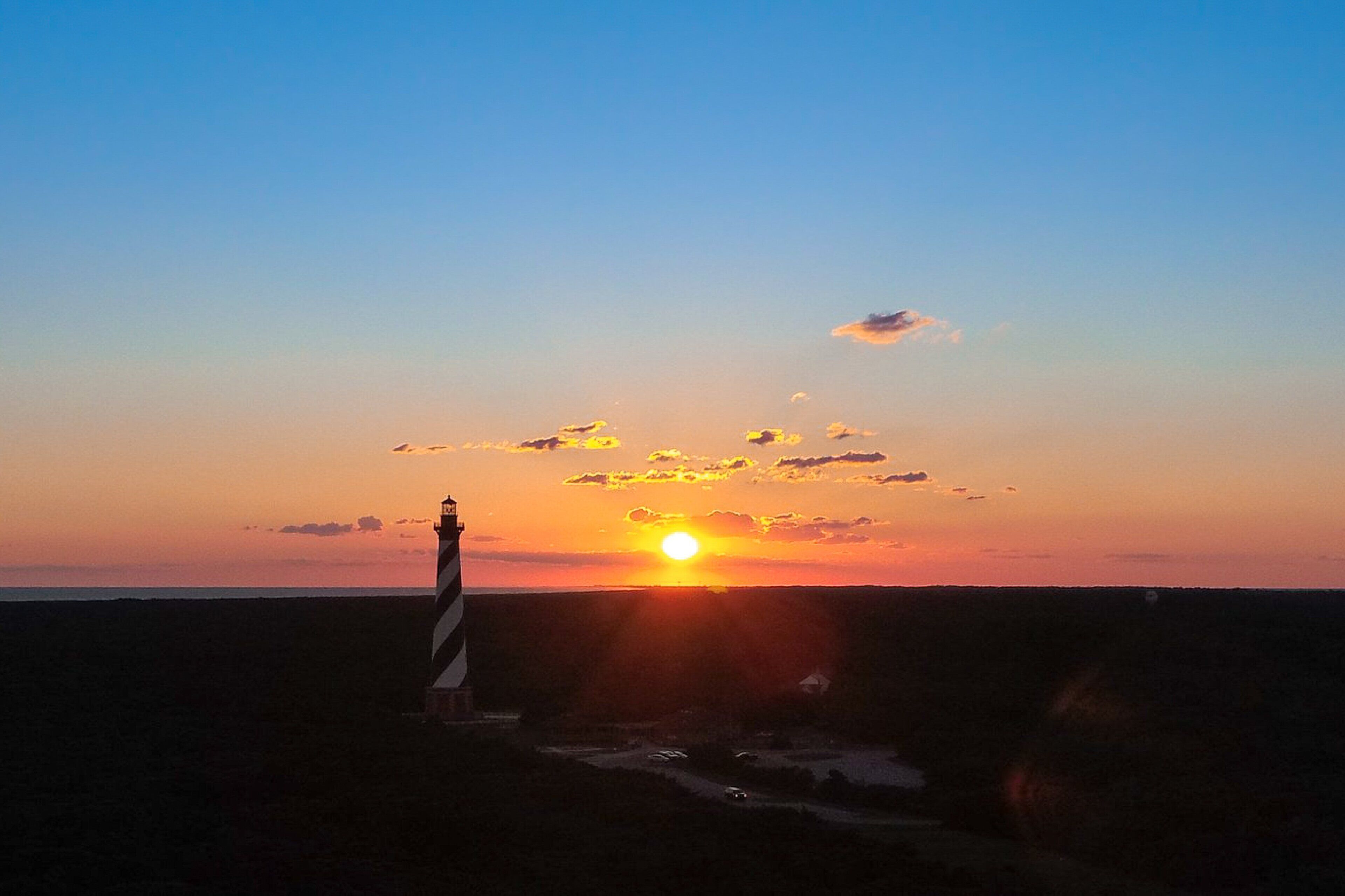 A lighthouse at sunset with the sun setting behind it.