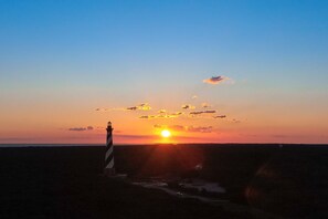 A lighthouse at sunset with the sun setting behind it.