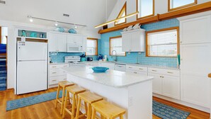 A modern kitchen with white cabinets, a blue backsplash, and a central island with stools.